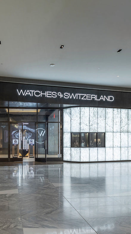 Watches of Switzerland storefront with illuminated signage and marble-patterned walls in a mall setting.