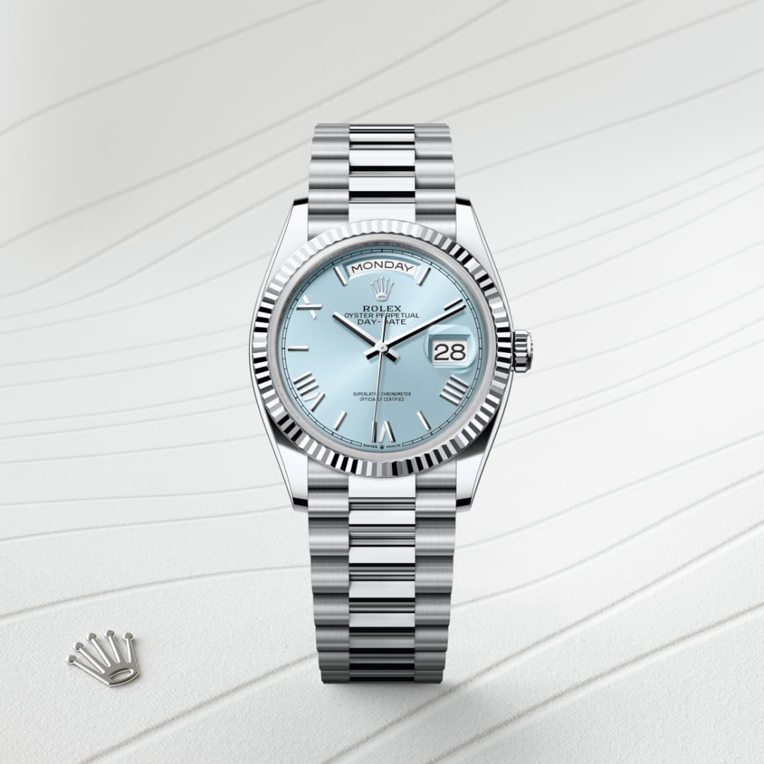 A silver Rolex watch with a light blue face displaying the day and date, set on a textured white background.