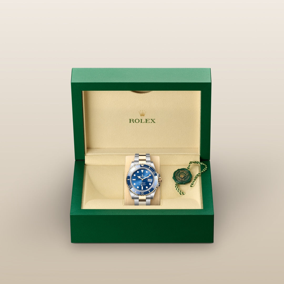 A Rolex watch with a blue face in a green and beige box, accompanied by a green tag.
