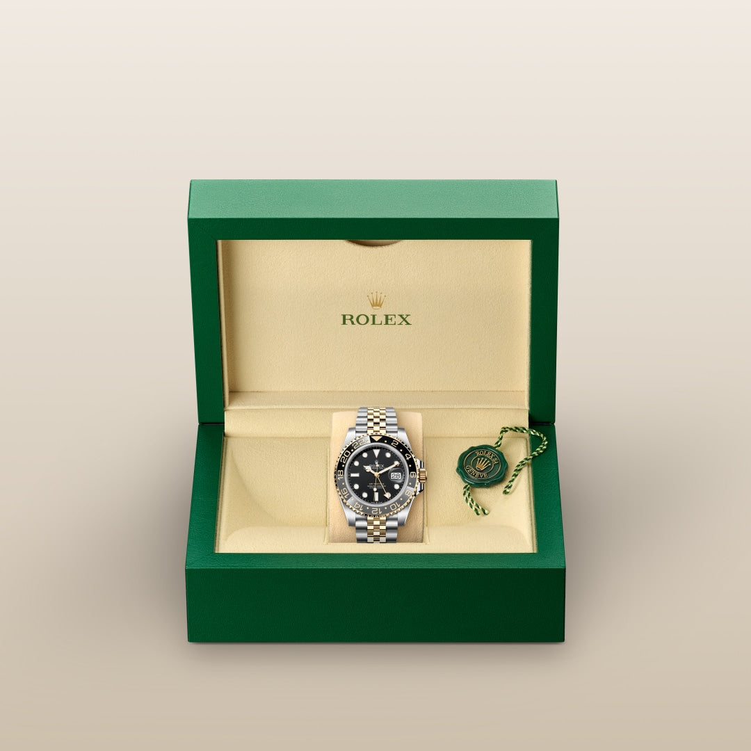 A Rolex watch with a silver band in a green and beige box, with a green tag beside it.