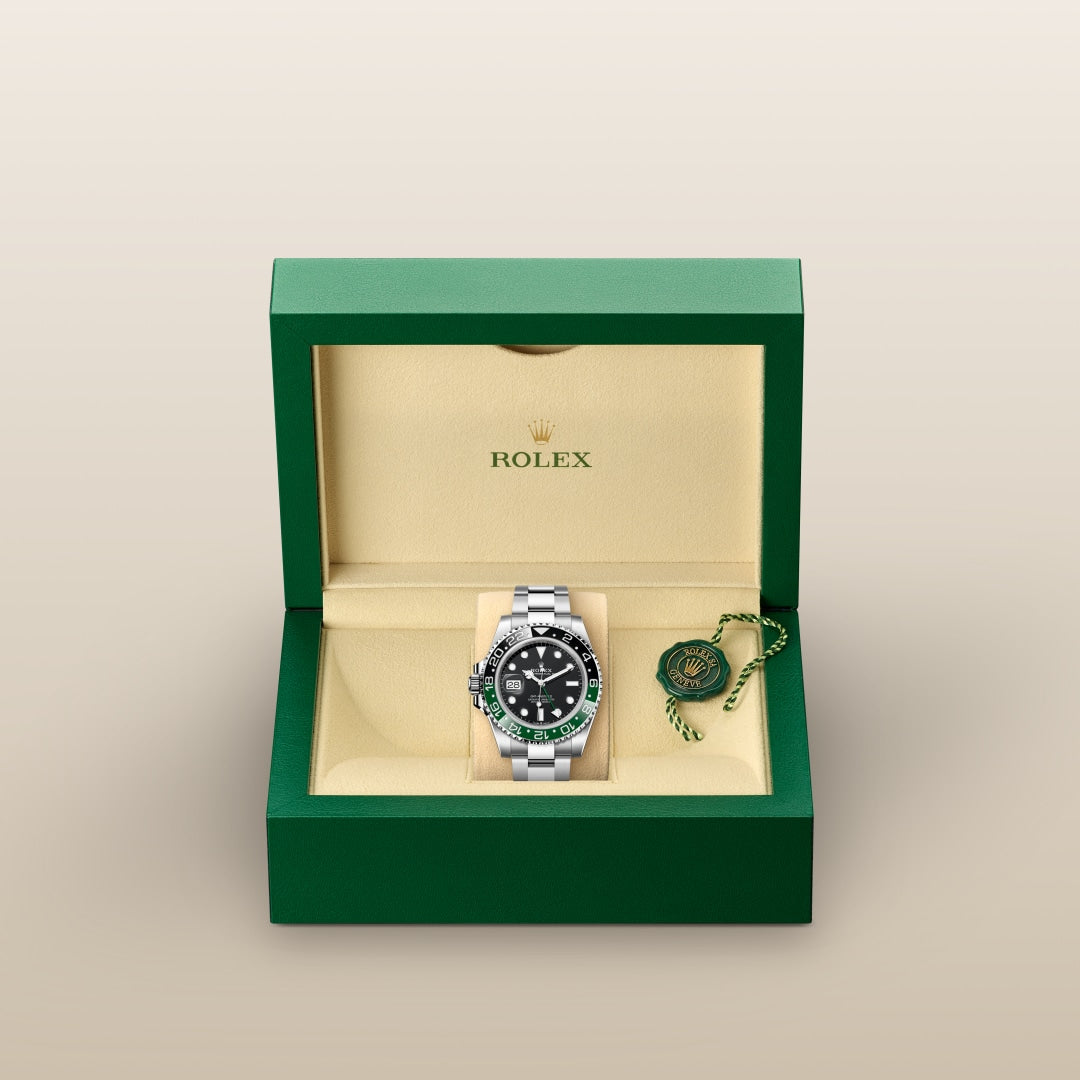 A Rolex watch with a black and green bezel in a green box with a tag, displayed against a plain background.