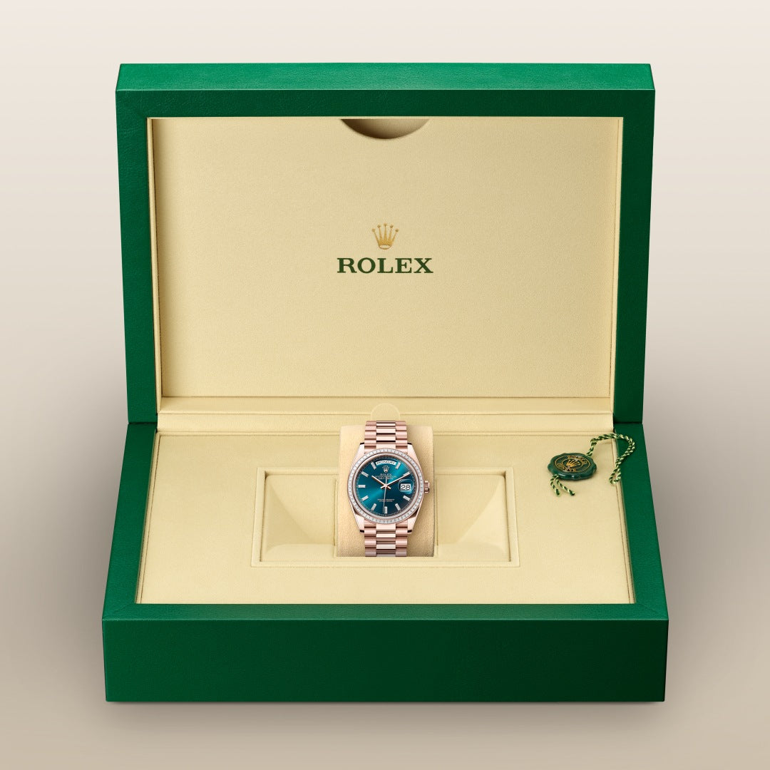 A Rolex watch with a green dial in a green and beige Rolex box, with a green tag on the side.