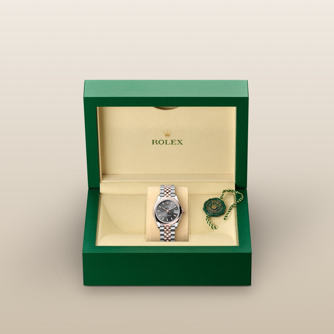 A Rolex watch with a silver band and black face displayed in an open green and beige Rolex box.