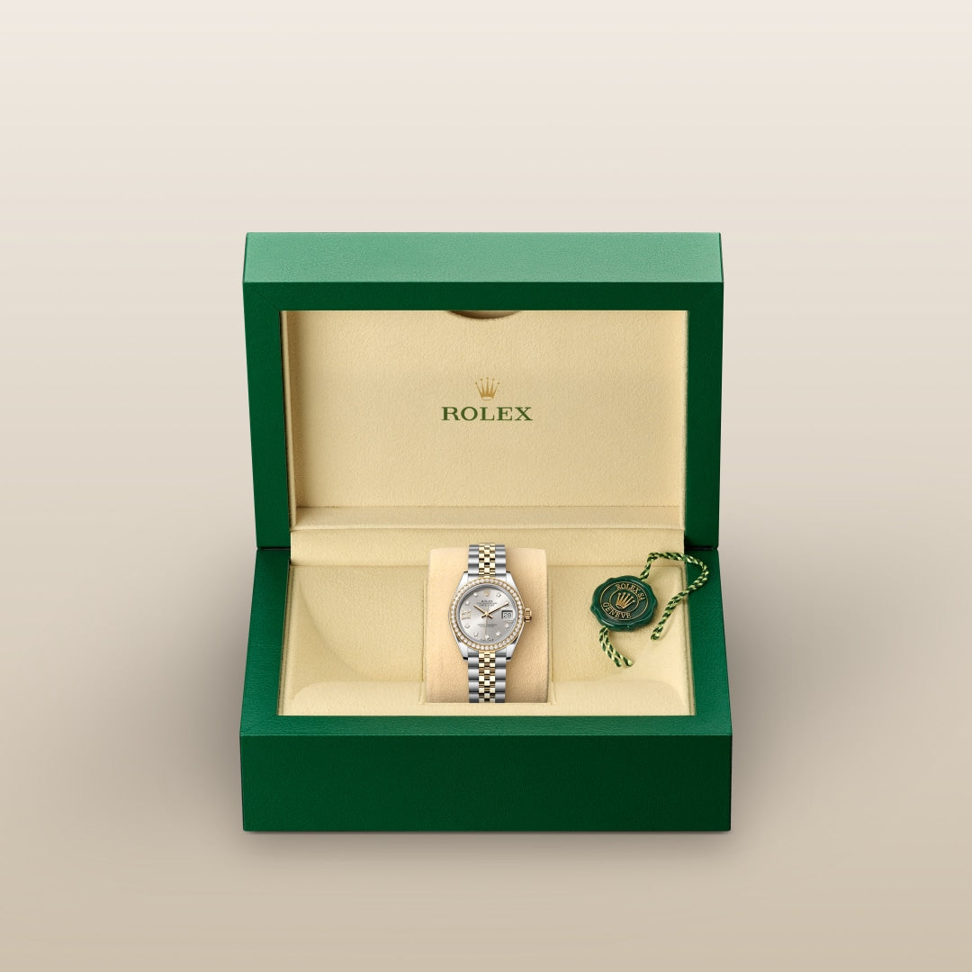 A Rolex watch with a silver and gold band in a green and beige Rolex box with a green tag inside.