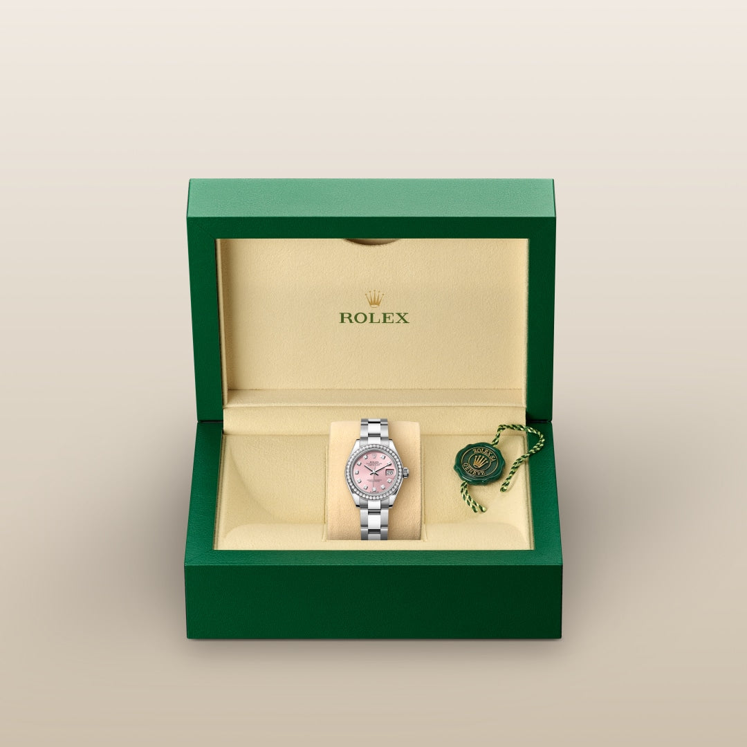A silver Rolex watch with a pink face in a green and beige Rolex box with tag.
