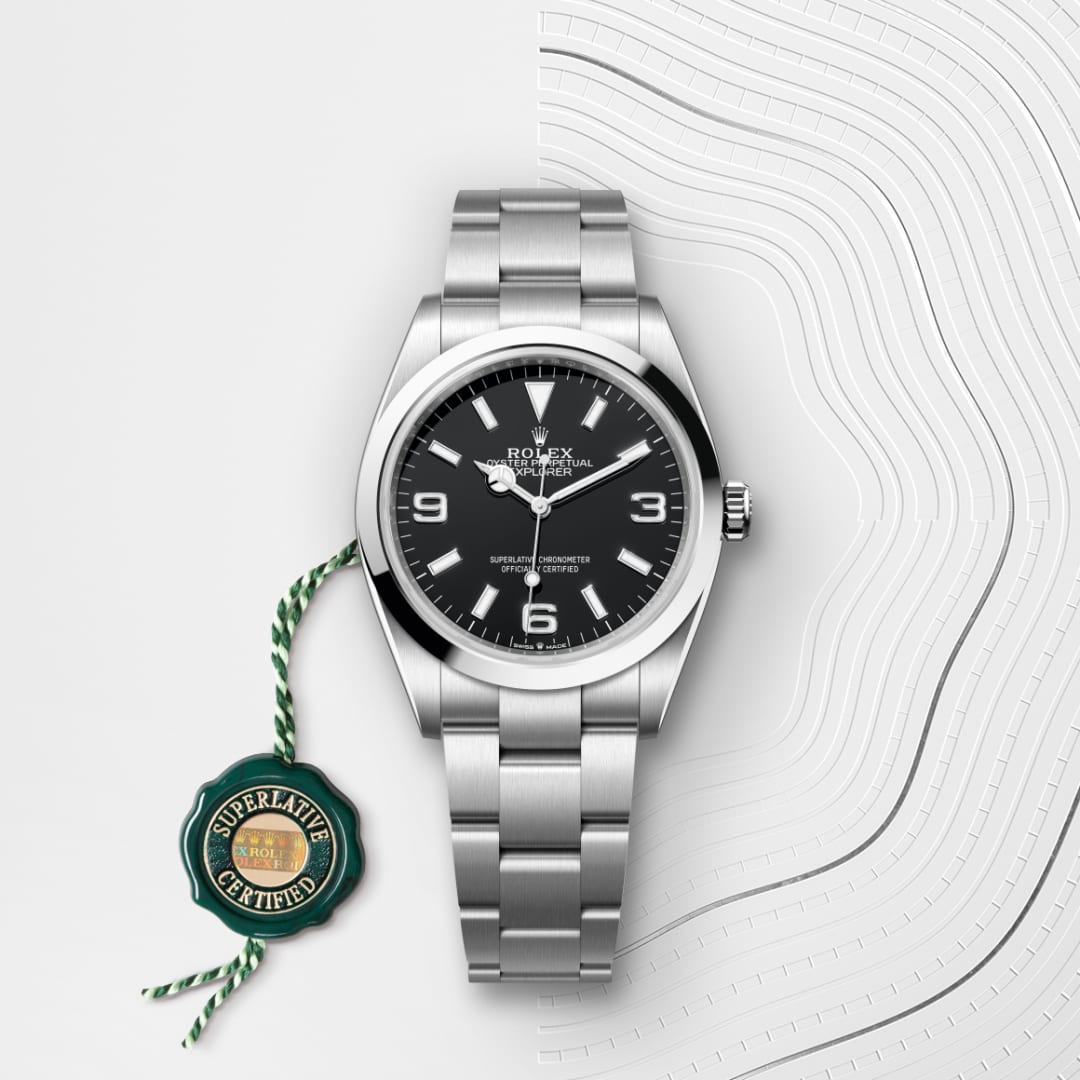A silver Rolex watch with a black dial and green tag, displayed on a textured white background.