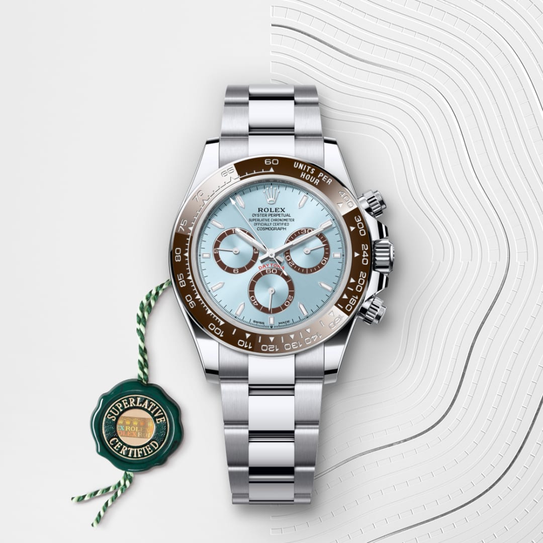A silver Rolex watch with a light blue face and brown bezel, next to a green Superlative Certified tag.