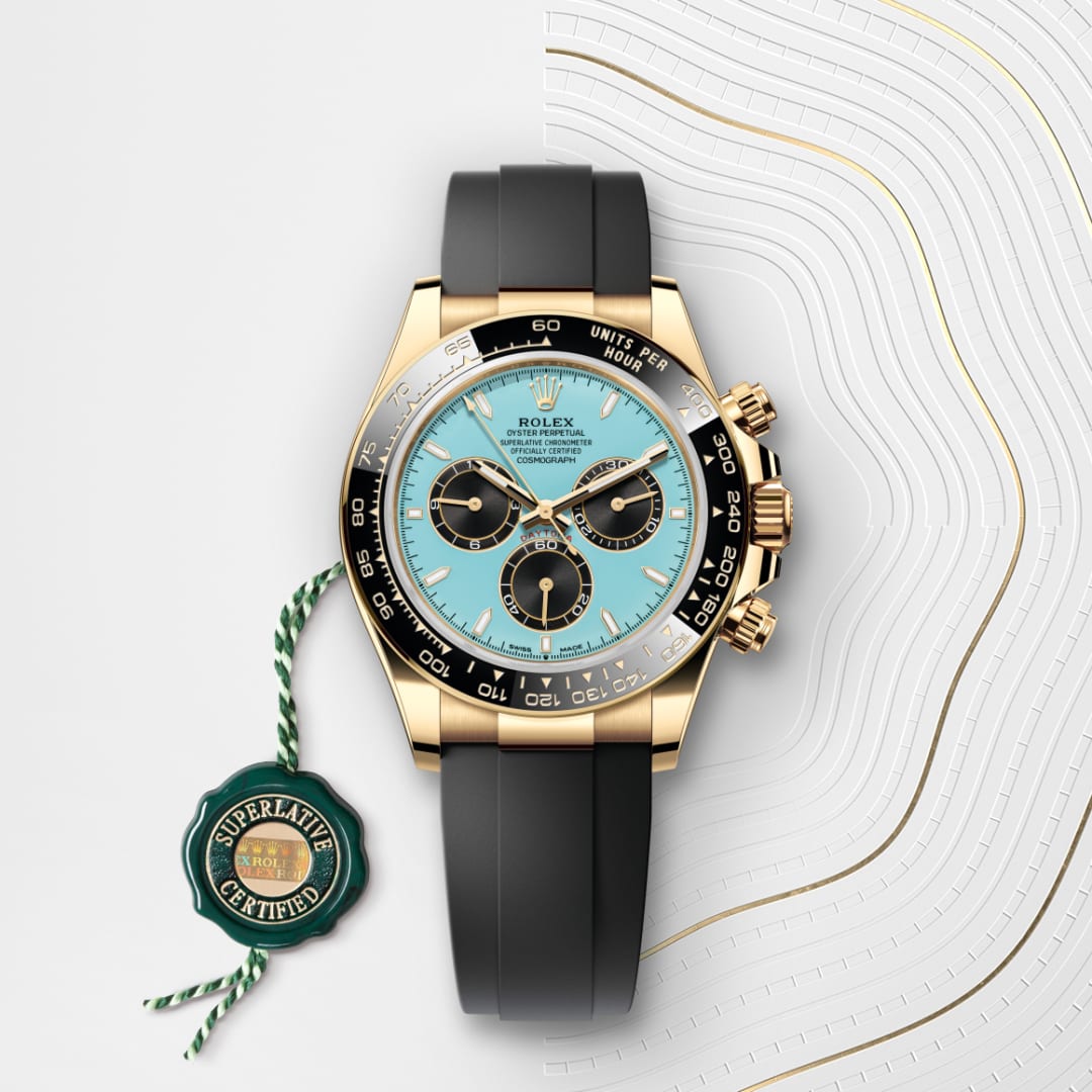 Rolex gold watch with turquoise dial, black subdials, black band, and green Superlative Certified tag.