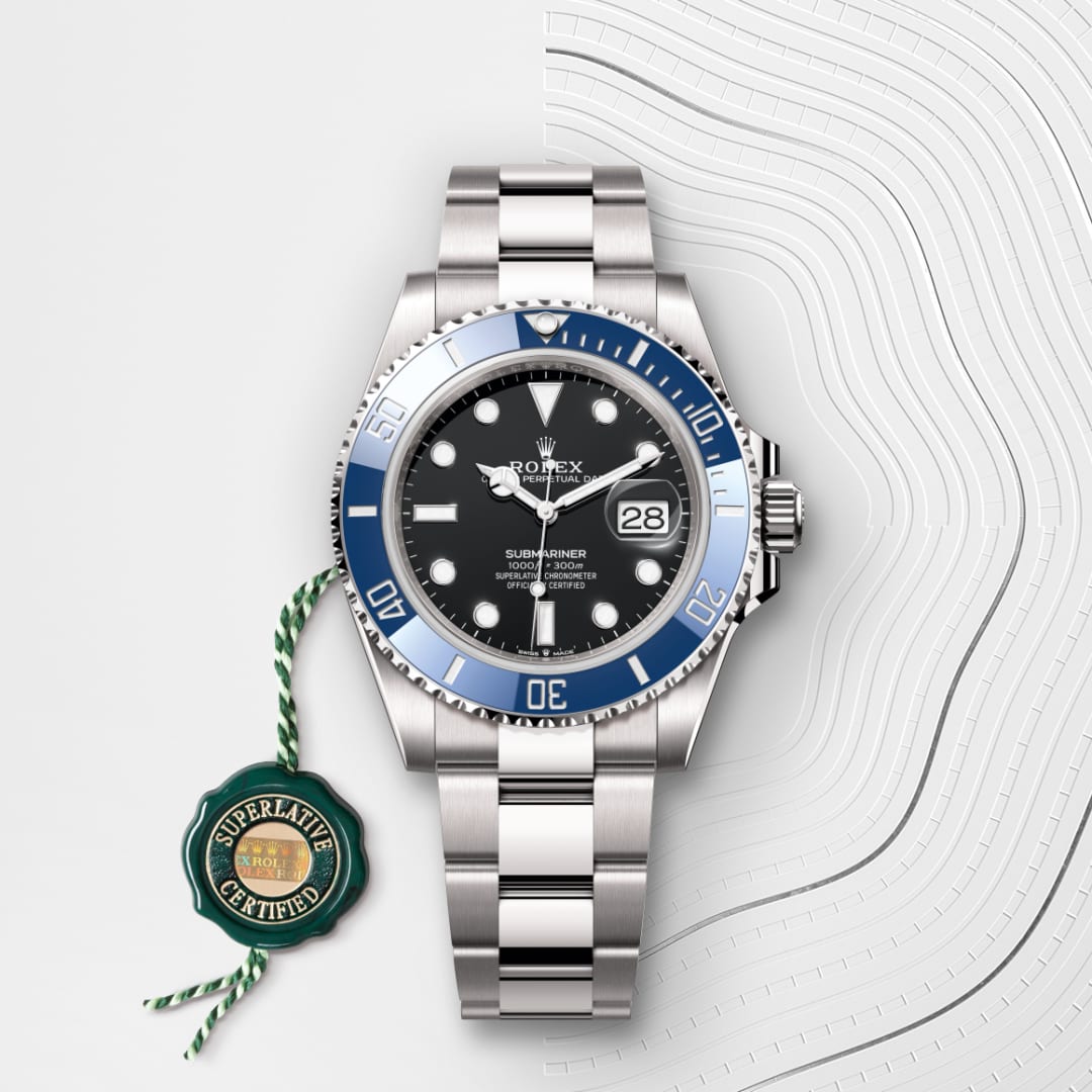A stainless steel Rolex Submariner watch with a blue bezel and black dial, displayed on a white patterned background.