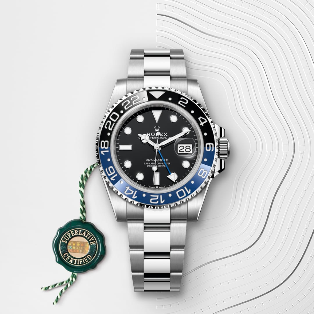 A silver Rolex watch with a black and blue bezel and a green Superlative Certified tag on a white background.