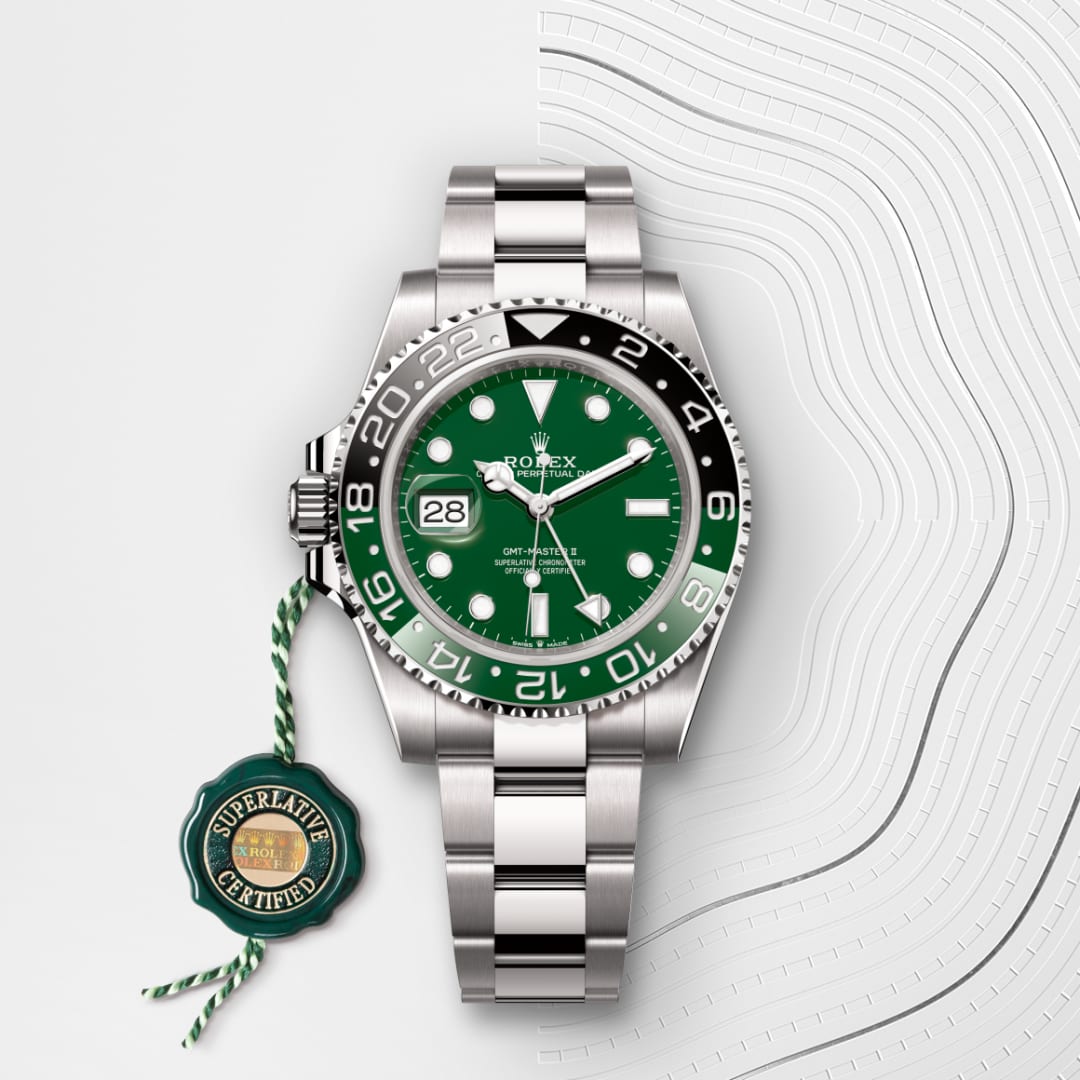 A silver Rolex watch with a green face and a green Superlative Certified tag on a white patterned background.