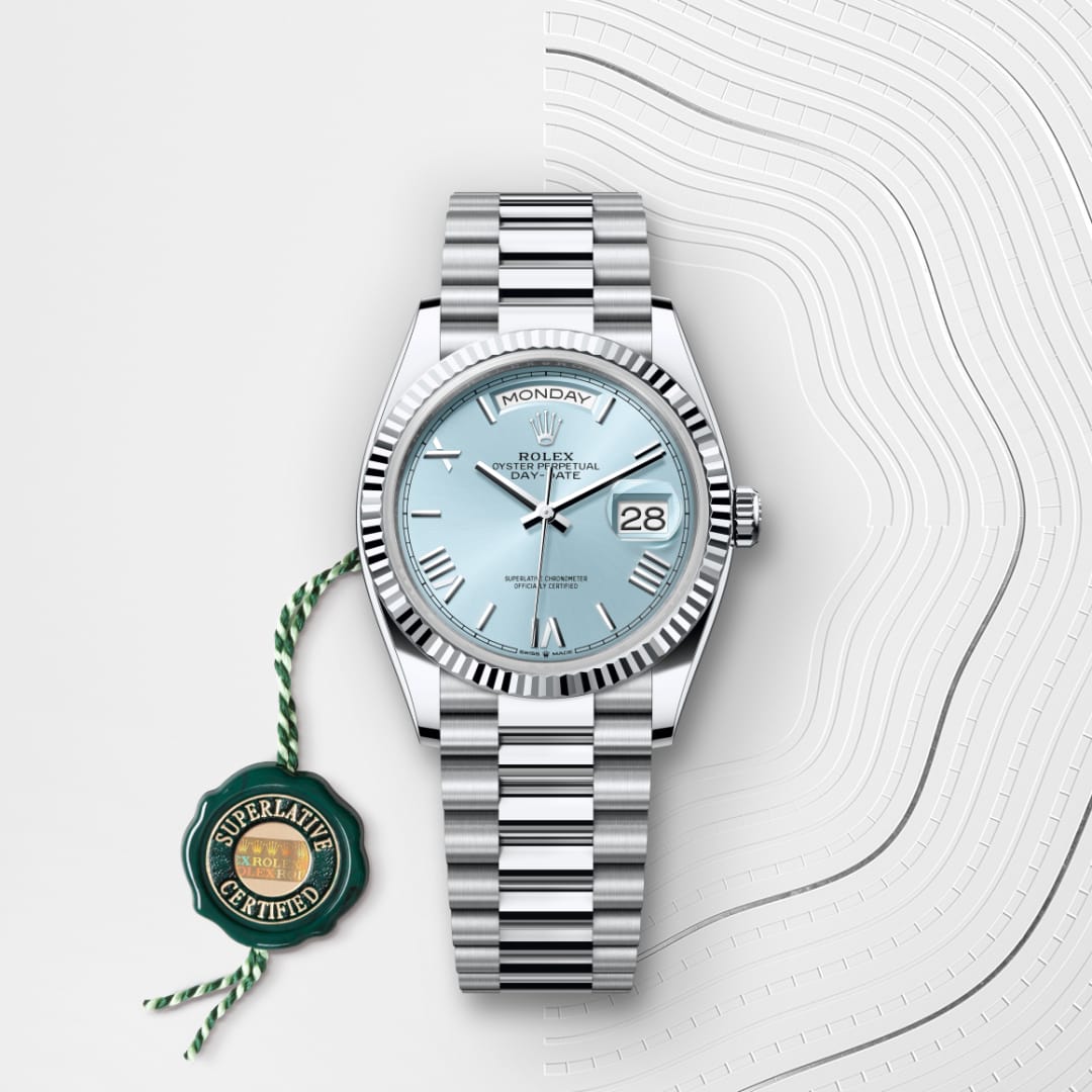 A silver Rolex watch with a light blue face and date display, next to a green Superlative Certified tag.