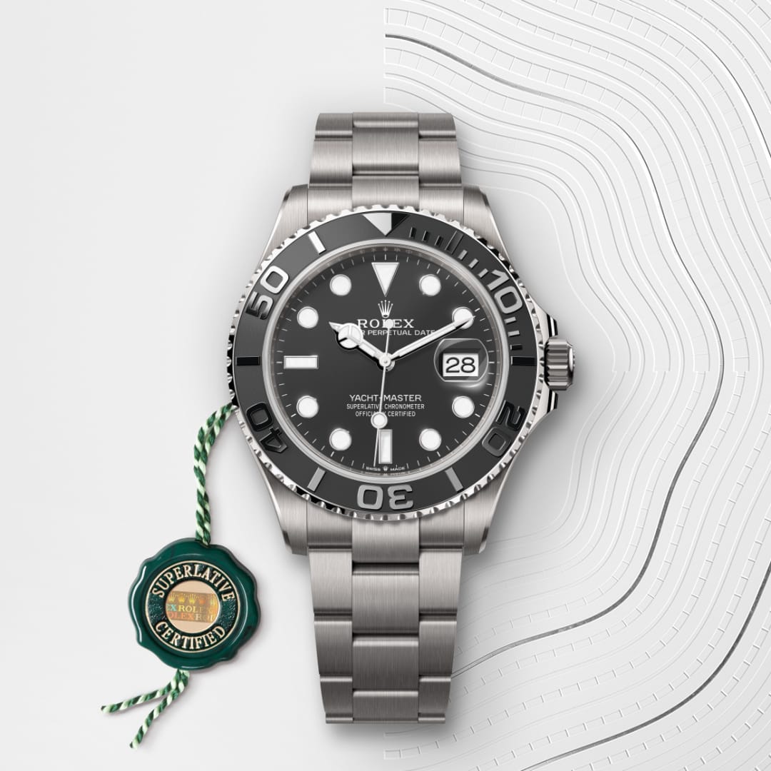 A silver Rolex Yacht-Master watch with a black dial and date display, next to a green certification tag.