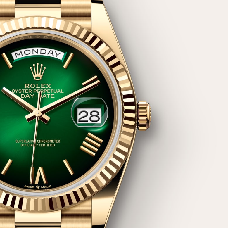 Close-up of a gold Rolex watch with a green face, showing Monday and the date 28.