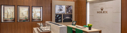 Modern Rolex showroom with wooden walls, display cases of watches, and branded décor on the wall.