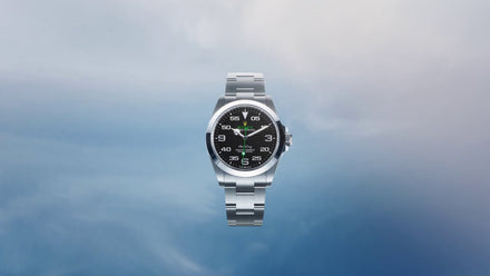 A silver wristwatch with a black dial floats against a light blue, cloudy background.