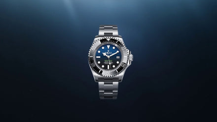 A silver luxury wristwatch with a black dial and bezel, displayed against a dark blue gradient background.