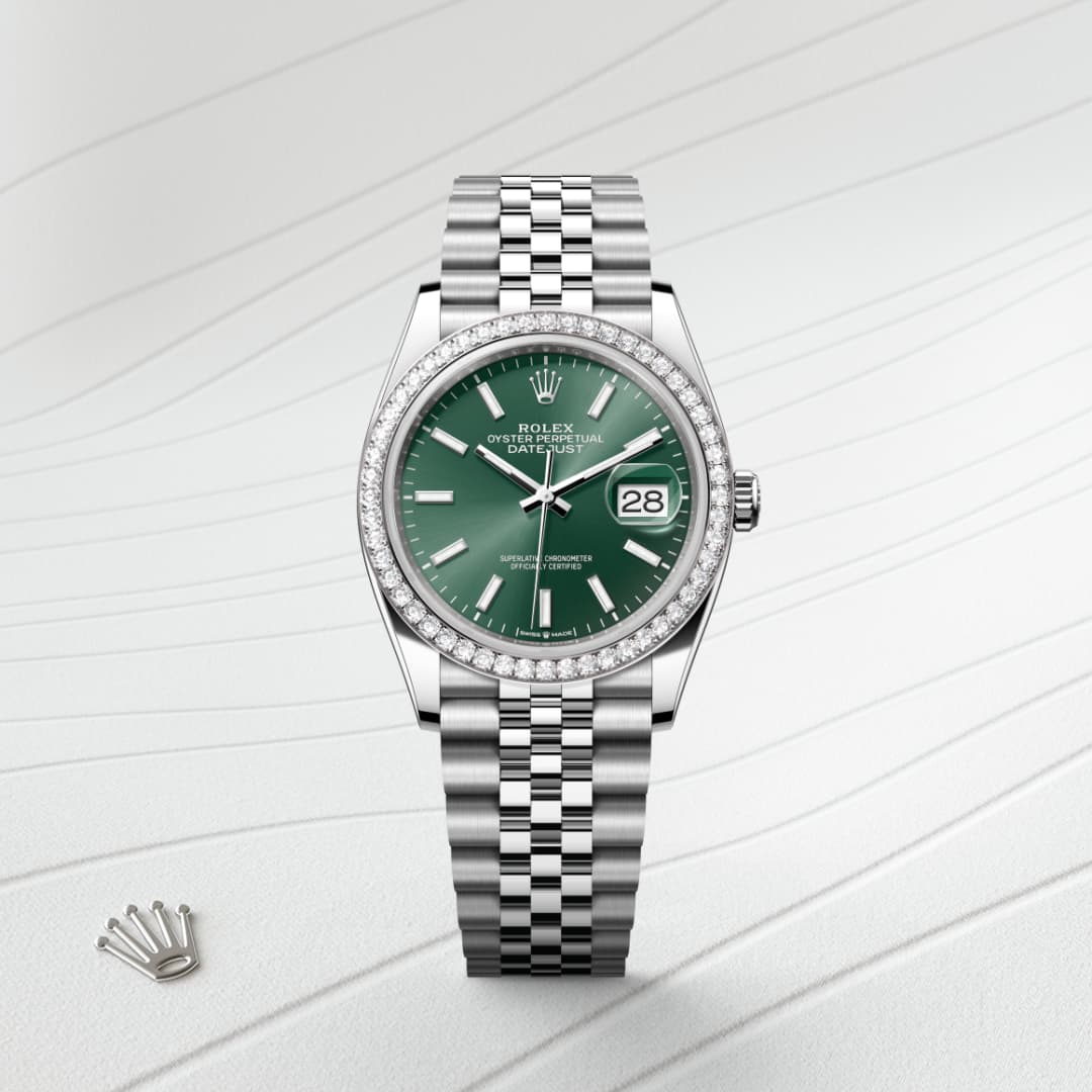 A silver Rolex watch with a green face, diamond bezel, and date display on a textured white background.