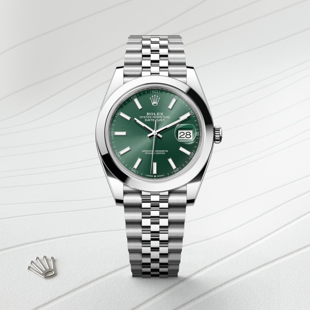 Silver Rolex watch with a green face and date display, set on a textured white background with a small crown logo.