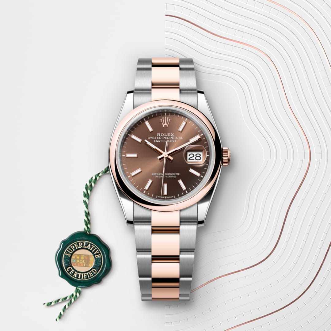 A two-tone Rolex watch with a brown dial and date display, next to a green “Superlative Certified” tag.