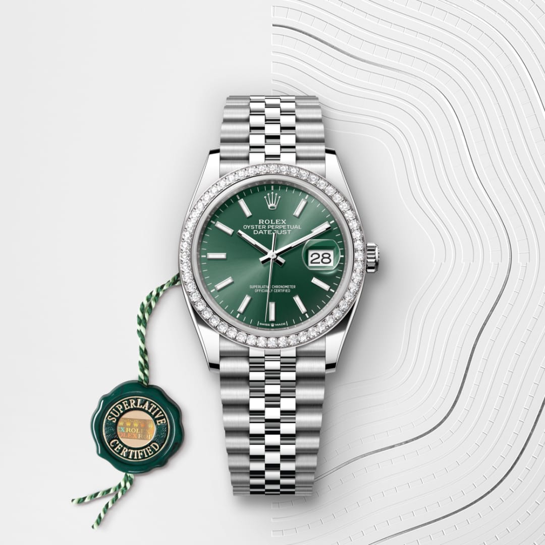 A Rolex Datejust watch with a green dial, diamond bezel, and metal bracelet, next to a Superlative Certified tag.