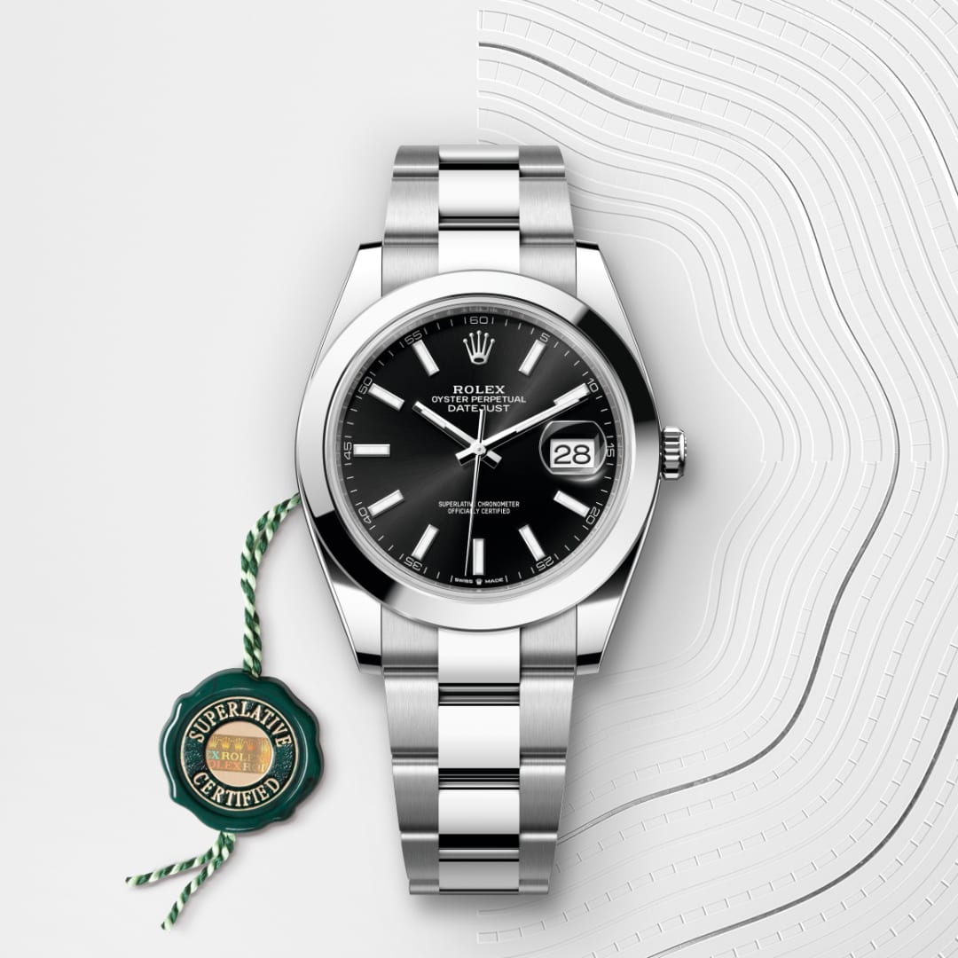 A silver Rolex Datejust watch with a black dial and date display, next to a green Superlative Certified tag.