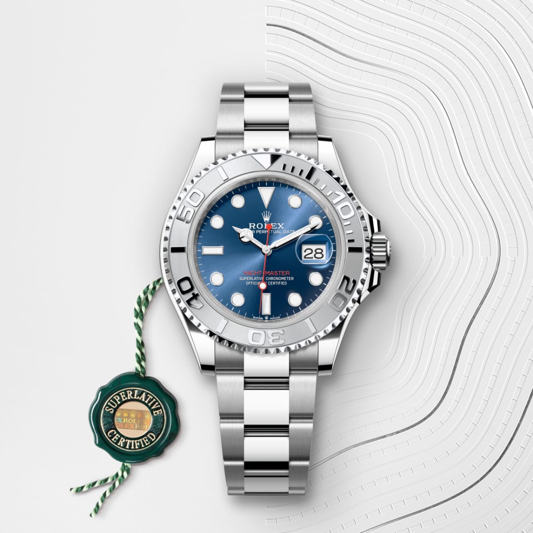 Silver Rolex watch with blue dial on a patterned white surface, next to a green Superlative Certified tag.