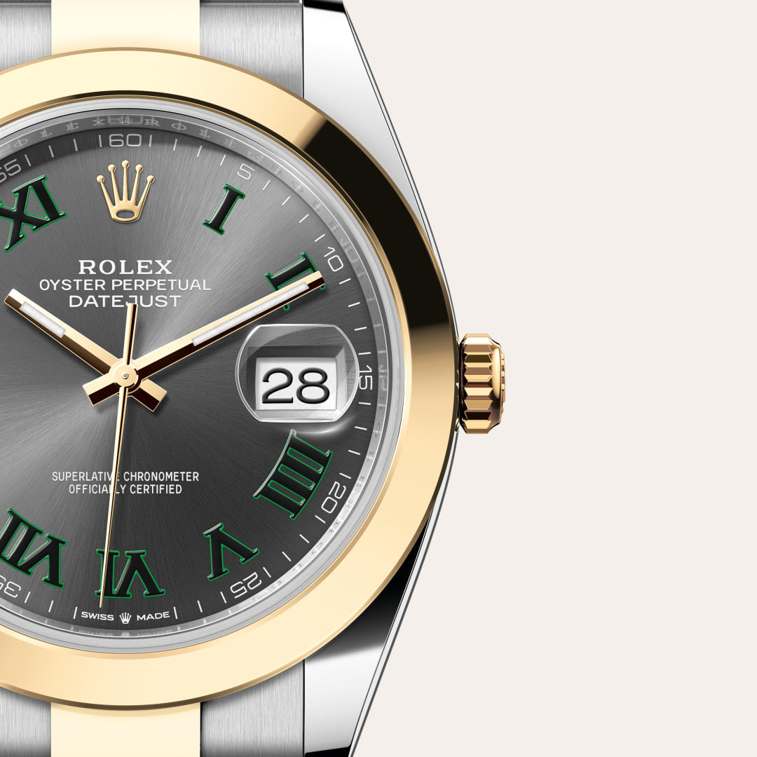 Close-up of a Rolex Datejust watch with a grey dial, gold bezel, and green Roman numerals, showing the date 28.