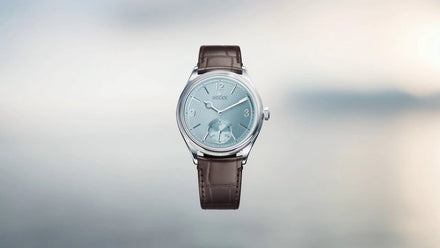 A silver wristwatch with a light blue face and brown leather strap on a blurred background.