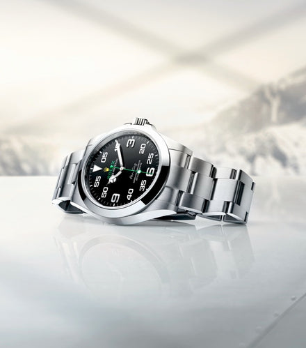 A silver wristwatch with a black dial and white numbers resting on a glossy surface.