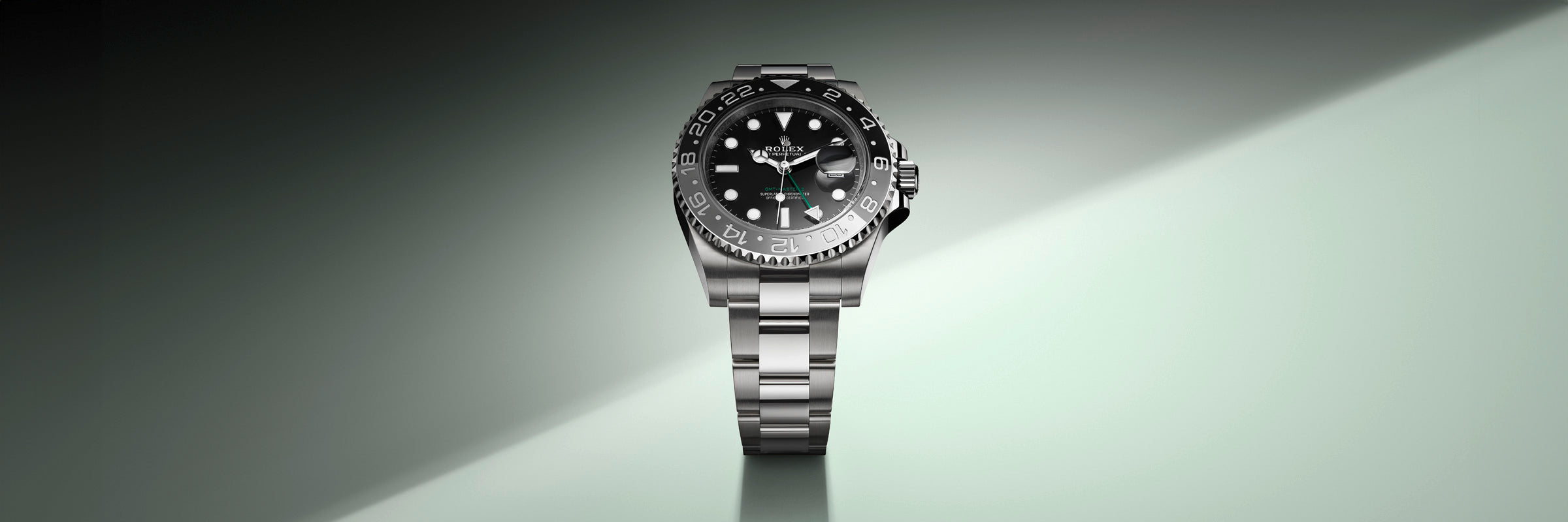 A silver luxury wristwatch with a black dial and bezel on a light green gradient background.