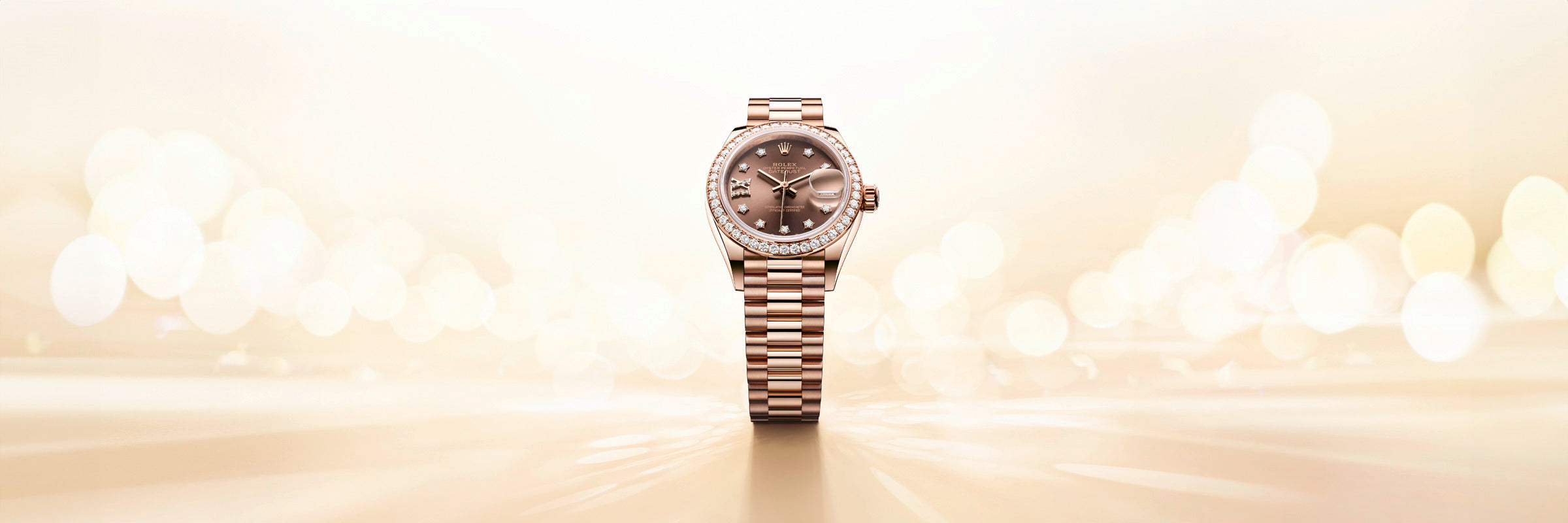 A rose gold wristwatch with a diamond bezel on a shiny, light-colored, blurred background.