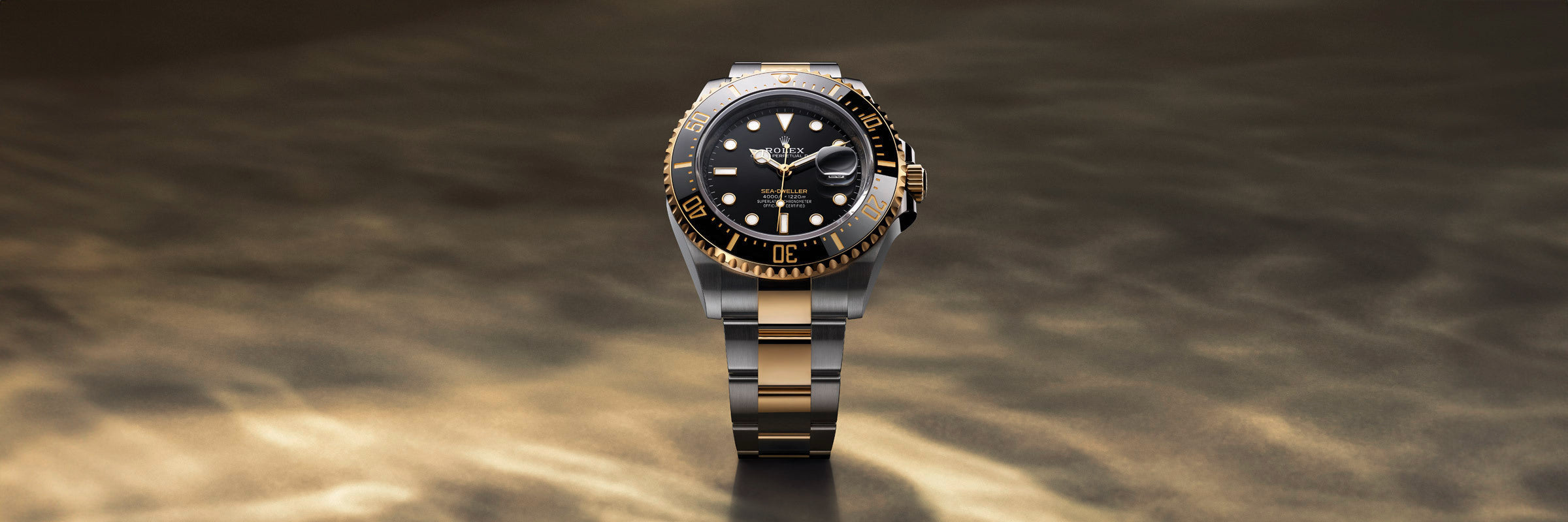 A luxury two-tone wristwatch with a black dial and gold accents on a reflective, golden-brown surface.