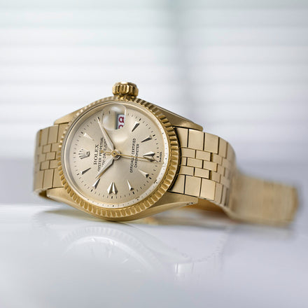 A gold Rolex wristwatch with a metal band is resting on a glossy white surface.