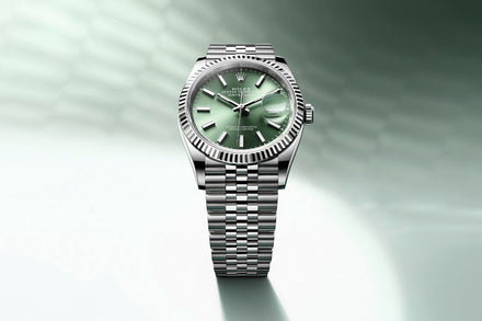 A silver Rolex watch with a green dial and metal link bracelet on a gradient green background.