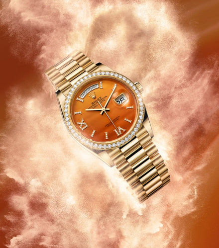 A gold watch with a diamond bezel and orange face, displayed against a swirling orange and gold background.