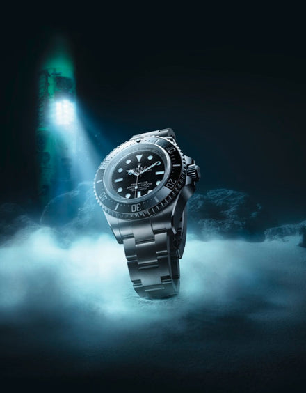 A silver luxury dive watch stands upright in misty water, illuminated by an underwater light.