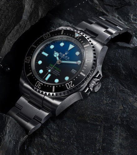 A Rolex Deepsea watch with a blue dial rests on dark, textured rocks.