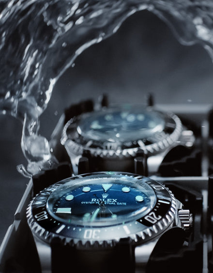 Close-up of two Rolex watches with water splashing above, highlighting their waterproof design.