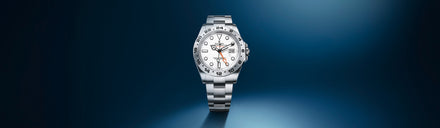 A silver Rolex watch with a white dial and metal band displayed on a gradient blue background.