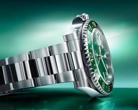 Close-up of a luxury stainless steel wristwatch with a green dial and bezel, set against a green background.