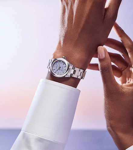 A person wearing a silver wristwatch with a white shirt, adjusting the watch on their wrist.