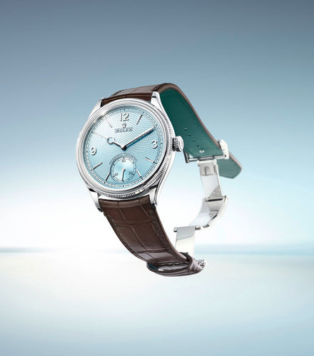 A silver Rolex watch with a blue face and brown leather strap, displayed against a light blue background.