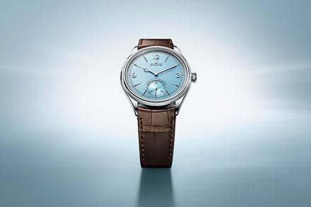 A silver watch with a light blue face and brown leather strap on a soft blue gradient background.