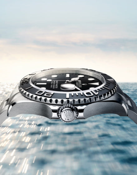 A close-up side view of a luxury watch with an ocean and sky in the background.