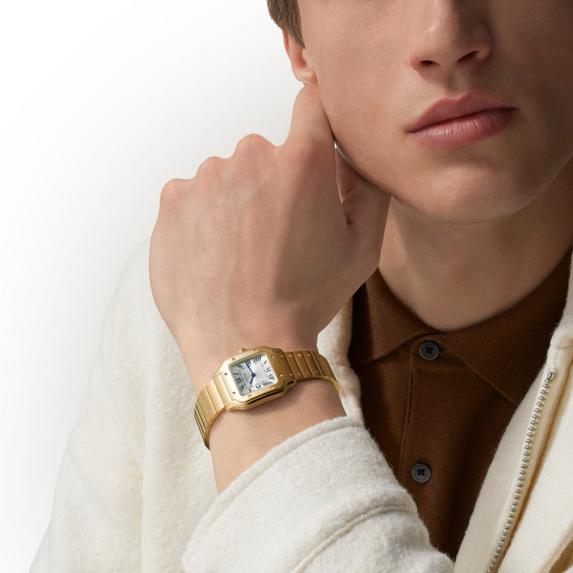 A person wearing a cream jacket and resting their chin on their hand, showcasing a Santos De Cartier Watch by Cartier.