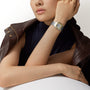 A woman in a sleeveless top and jacket showcases a Santos De Cartier Watch by Cartier on her left wrist.