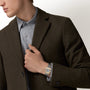 Person in a grey shirt and dark coat adjusts their jacket, showcasing a Santos De Cartier Watch by Cartier with a distinctive square face.