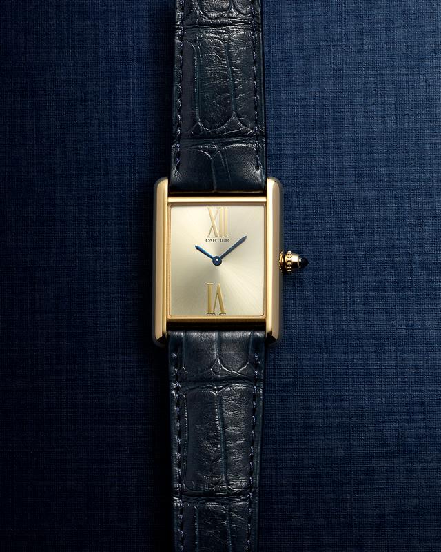 A gold rectangular wristwatch with black leather strap on a textured navy background.