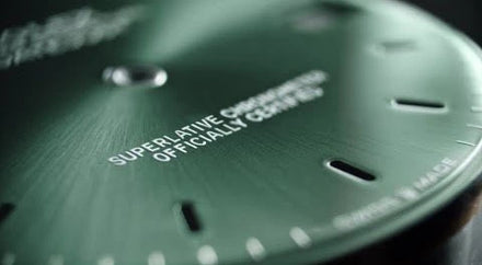 Close-up of a green watch face with Superlative Chronometer Officially Certified text in white.